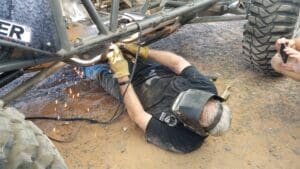 A man in black shirt and mask working on metal structure.