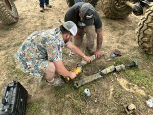 Two men working on a pipe in the dirt.