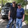 Two men standing next to a truck on the side of a road.