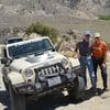 Two men standing next to a jeep on the side of a road.